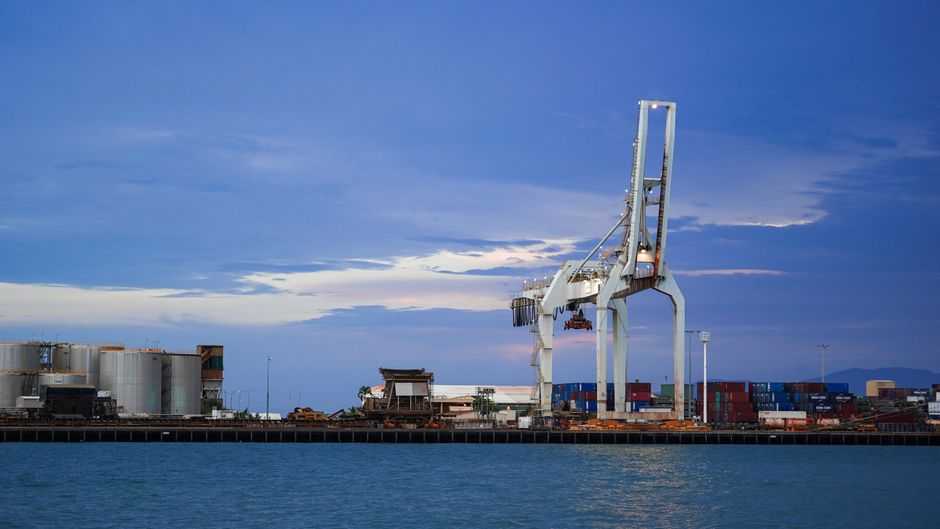 An industrial port terminal with cargo cranes and containers at twilight, representing the global shipping chokepoints disrupted by the US-Iran war.