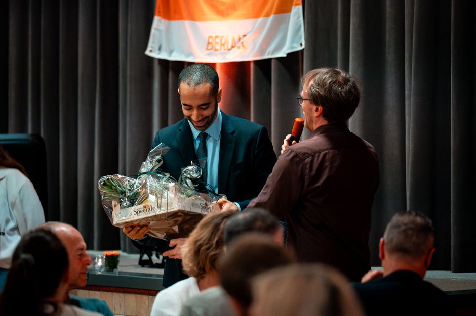 A man receiving a gift basket during an award ceremony indoors, evoking the celebratory atmosphere of a public listing event.