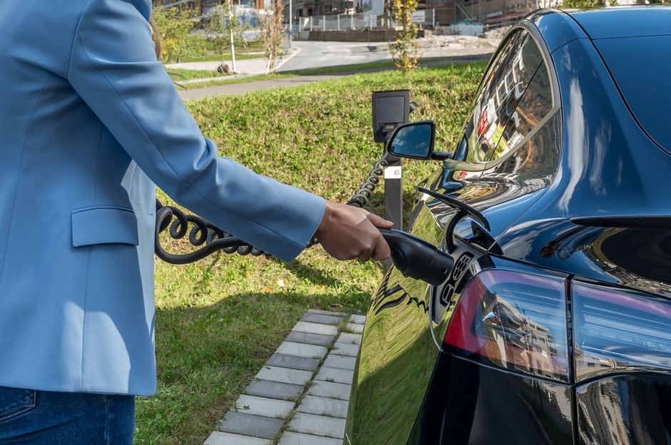 Person connecting an electric car to a charging station outdoors.