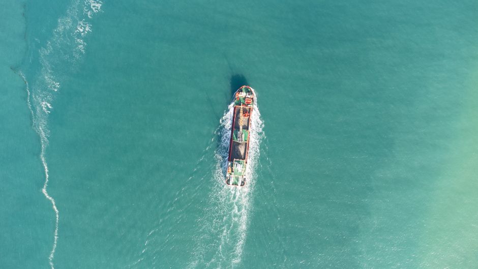 Drone shot of a cargo ship navigating through calm turquoise waters.