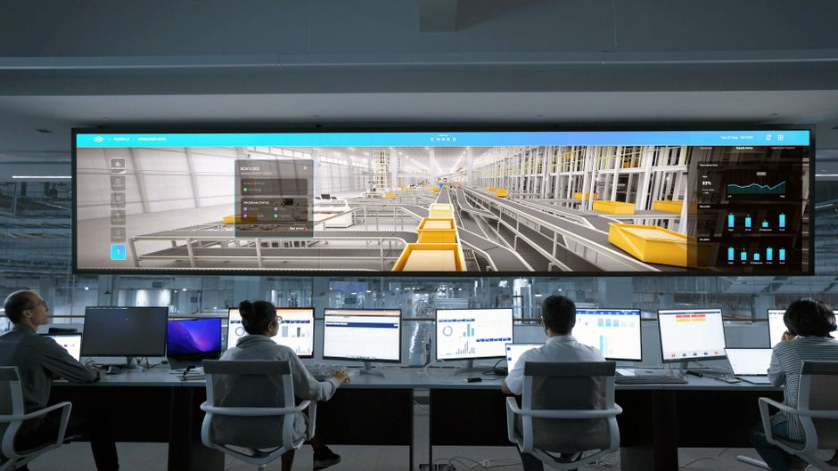 People monitor large digital displays and computer systems in a modern enterprise control room.