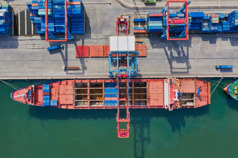Drone shot of cargo ship and containers at a port terminal, illustrating trade and transportation.