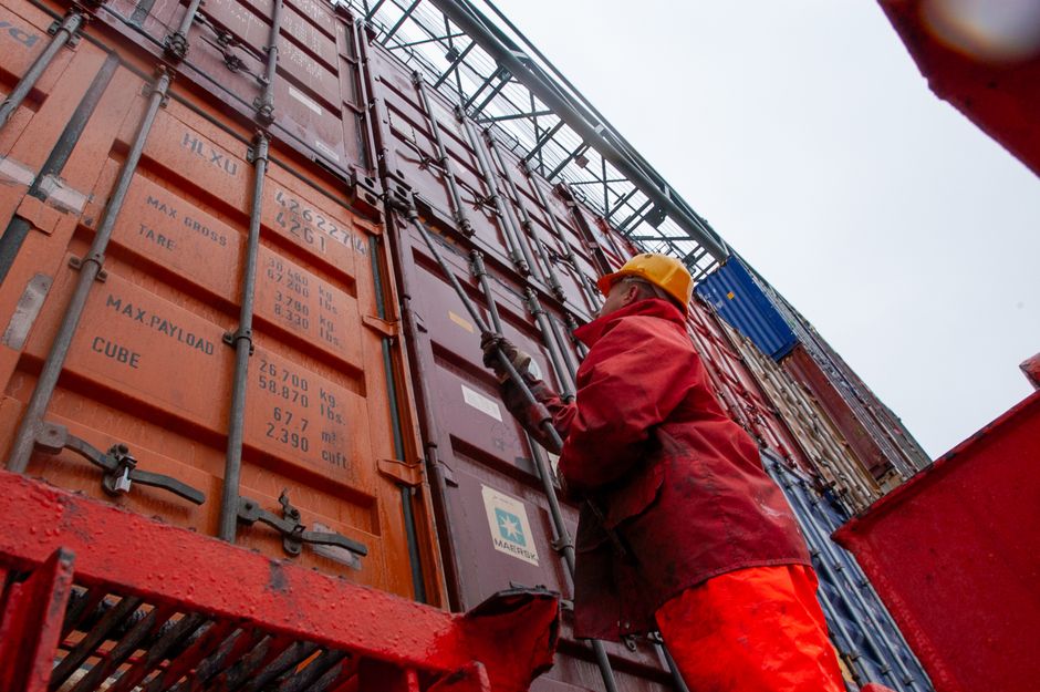 Worker securing shipping containers at a port in rainy weather