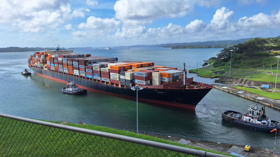 A cargo ship is guided through a narrow canal, representing the shipping chokepoints driving higher energy and logistics costs.
