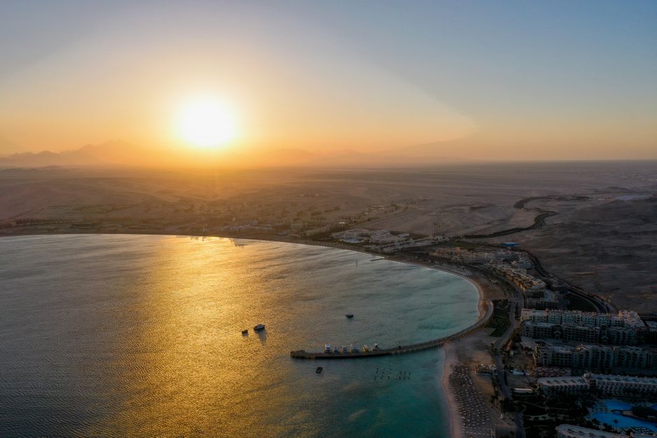 Aerial sunset view over a calm coastal bay with distant desert backdrop, evoking a Red Sea coastline