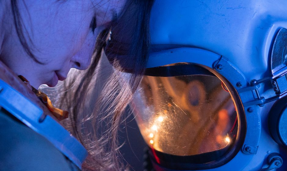 Close-up of a person wearing a blue spacesuit and helmet with a reflective visor.
