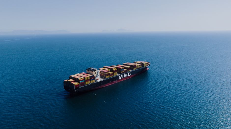 Aerial view of a loaded cargo ship sailing on open ocean waters under clear skies.