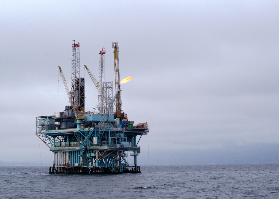 An offshore oil rig in the open sea with cranes and a gas flare against a cloudy sky, representing energy supply infrastructure