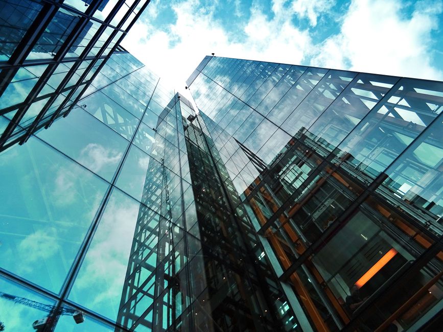 A modern glass skyscraper reflecting the sky and clouds, viewed from below.