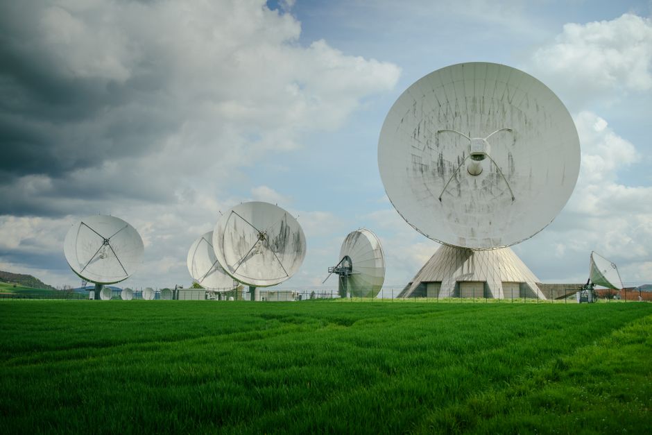 White parabolic satellite dish antennas in a green field under a cloudy sky