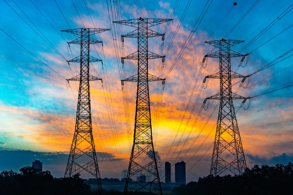 High voltage power transmission lines against a dramatic sunset sky, representing the energy infrastructure underpinning the AI build-out.