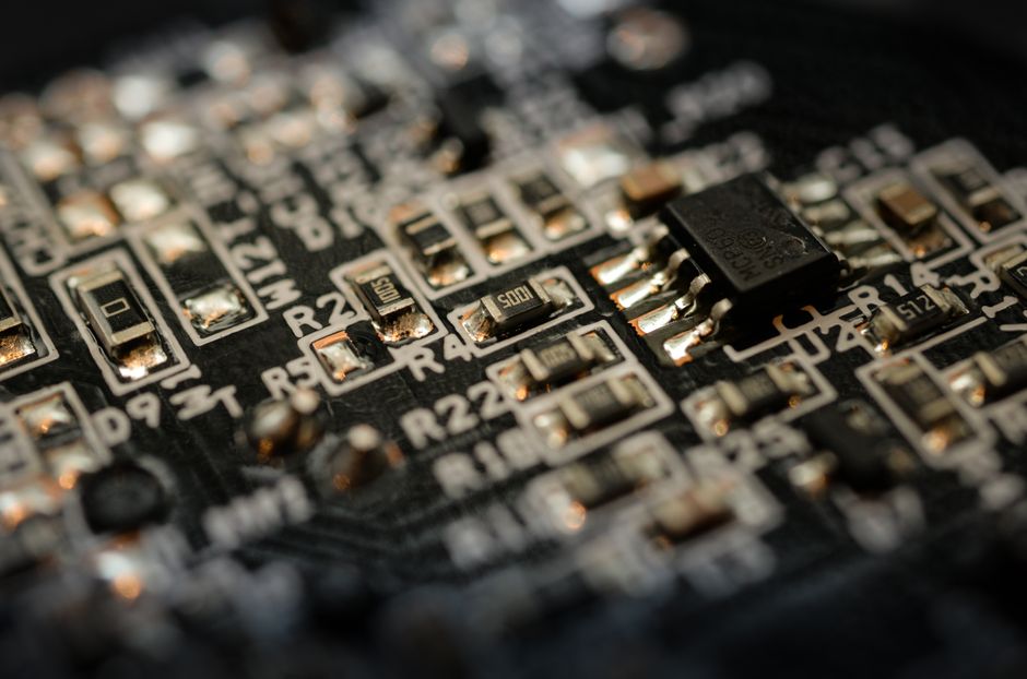 Close-up of a black semiconductor circuit board with microchips, capacitors, and fine gold trace connections, representing memory chip manufacturing.