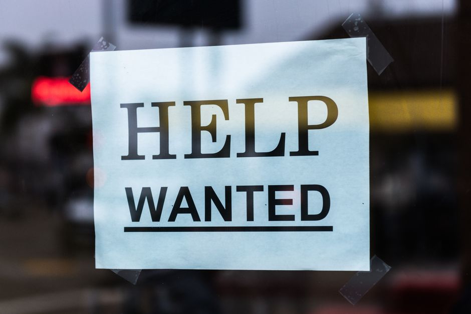 Help Wanted sign taped to a glass window in a storefront