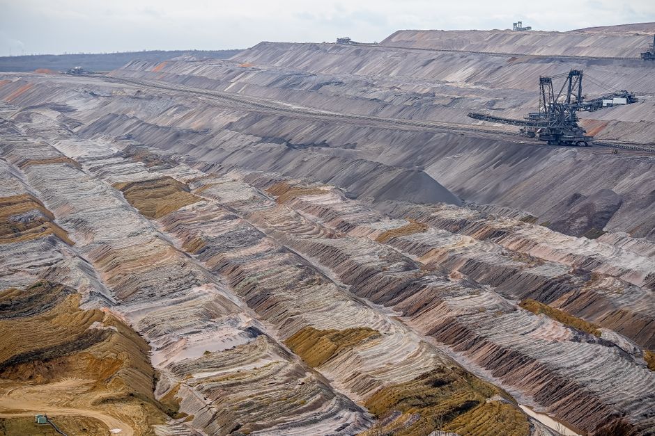 Aerial view of a large open-pit mine with machinery and textured soil layers, illustrating raw material extraction at industrial scale.