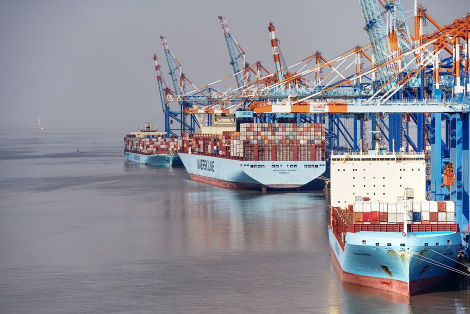 Container ships docked at a busy port with cranes and clear skies.