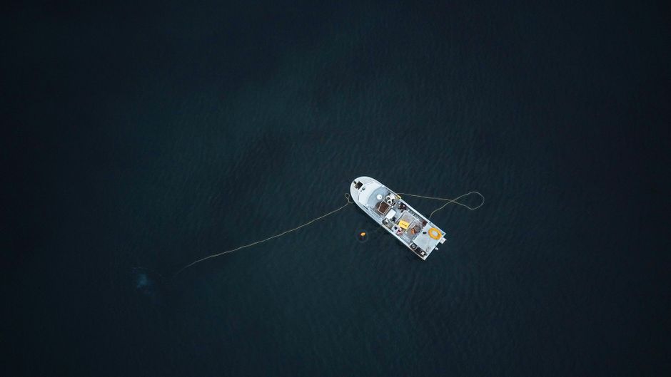 Aerial photograph of a single vessel anchored in a vast, dark ocean.