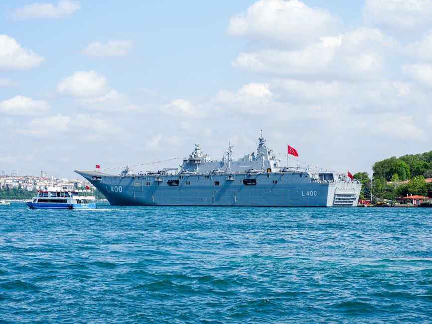 A Turkish naval warship navigates a strait on a sunny day.