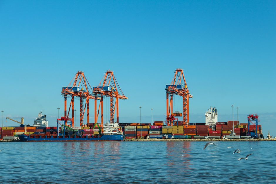 A vibrant container port with large cargo cranes and ships against a clear sky.