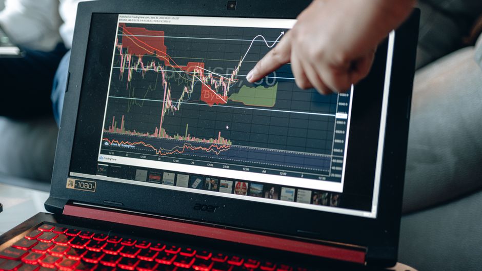 A person points at a financial chart on a laptop screen, analyzing stock market trends for investment decisions.