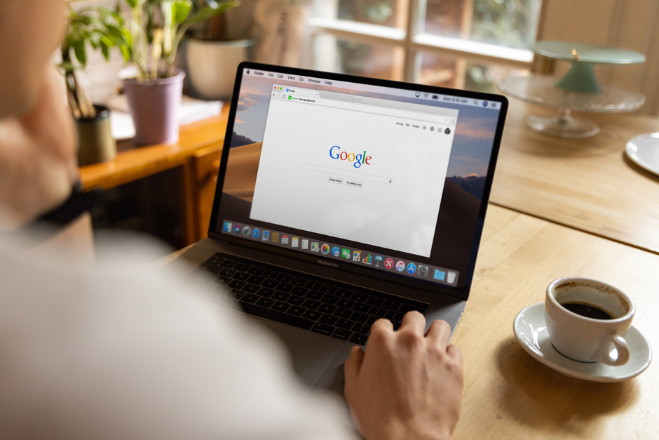 A person browsing Google on a laptop at a wooden table, illustrating everyday digital engagement with Alphabet's services.