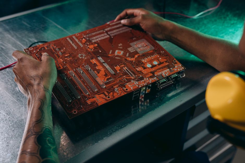 A technician's hands working on a green circuit board with electronic components