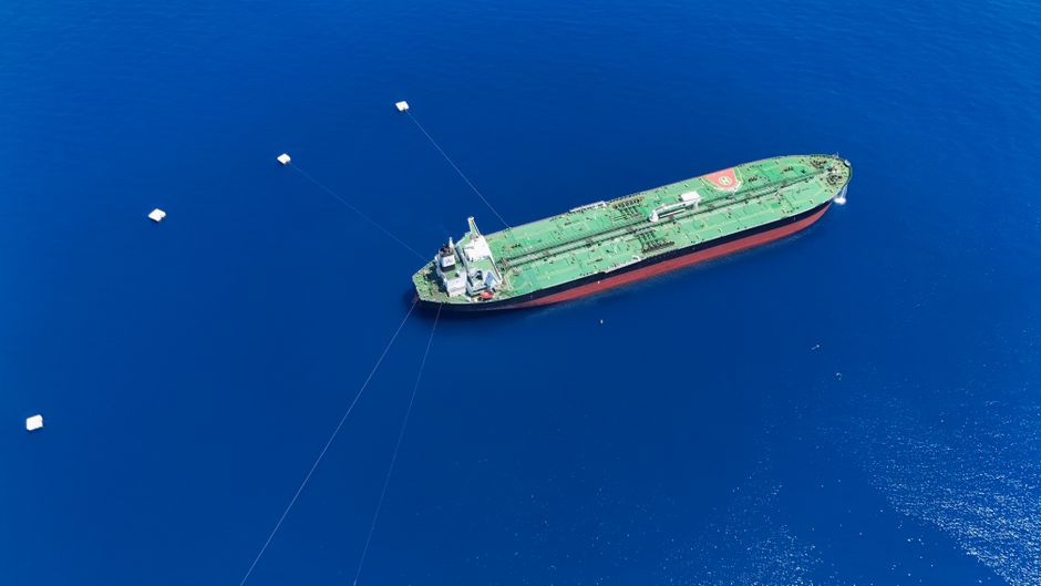 Aerial view of a tanker ship anchored in the open sea, illustrating the commercial shipping paralysis at Gulf chokepoints