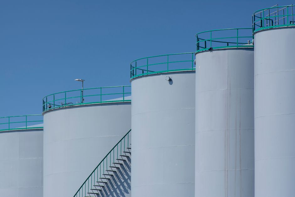 Large industrial storage tanks with green railings against a clear blue sky