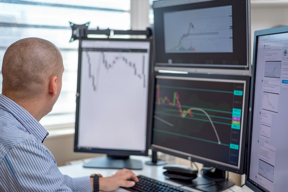 Trader analyzing financial data on multiple monitors in an office setting