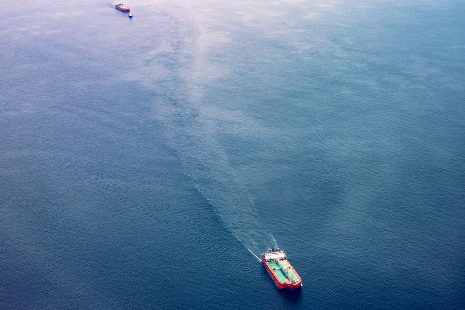 Two cargo ships navigate the vast blue ocean, representing the maritime trade routes passing through threatened chokepoints.