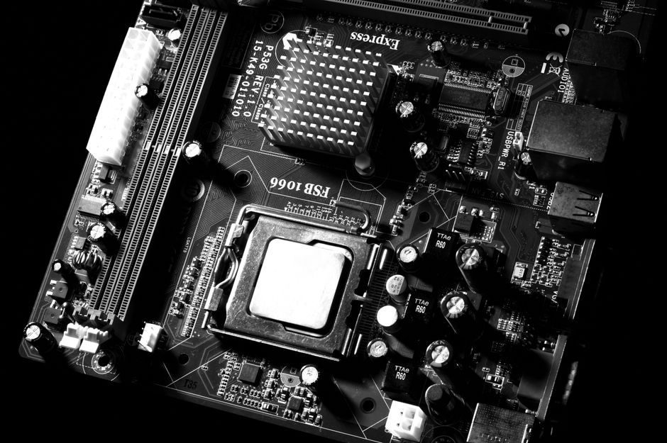 Monochrome close-up of computer motherboard circuitry with intricate electronic components and copper traces, representing semiconductor technology