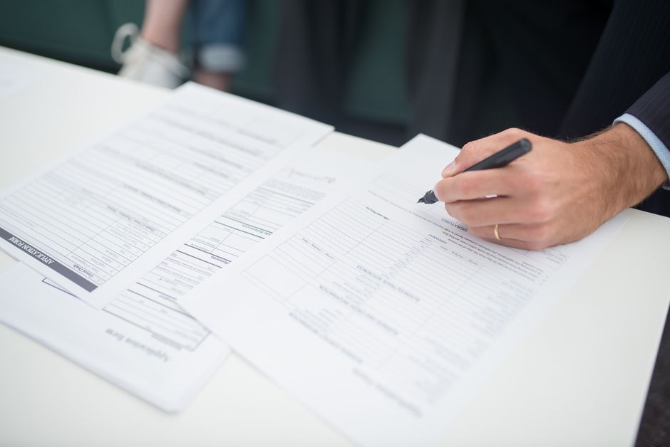 Close-up of a hand signing documents with a pen on a desk in an office setting.