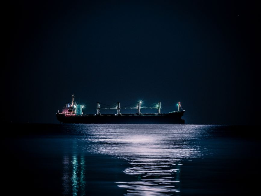 A cargo ship sailing on the ocean at night, illustrating the vulnerable crude shipping routes now threatened by Red Sea and Hormuz disruptions.