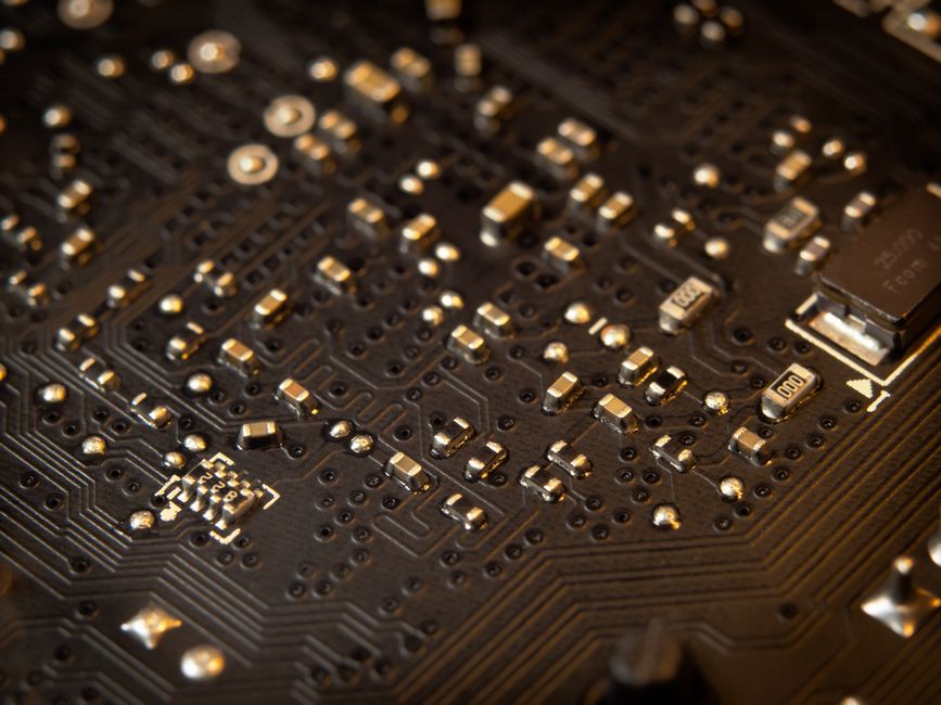 Close-up of a circuit board showing electronic components and copper traces, representing the semiconductor industry under pressure