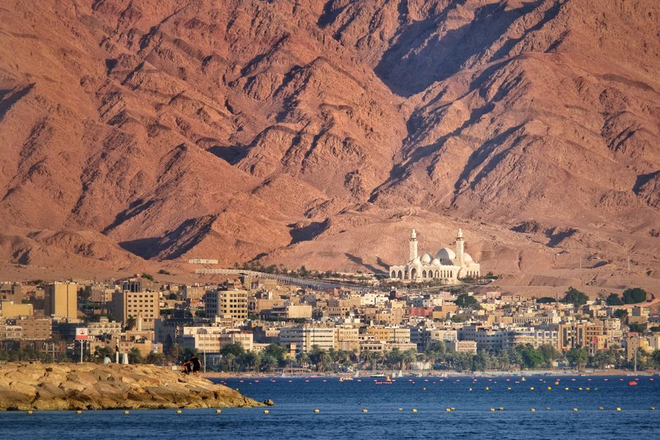 Coastal Red Sea city of Aqaba with dramatic desert mountains rising behind the waterfront, illustrating the strategic geography of the Bab al-Mandeb chokepoint.