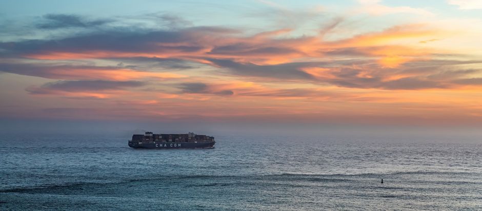 A large cargo container ship sailing across the ocean under a golden sunset sky.