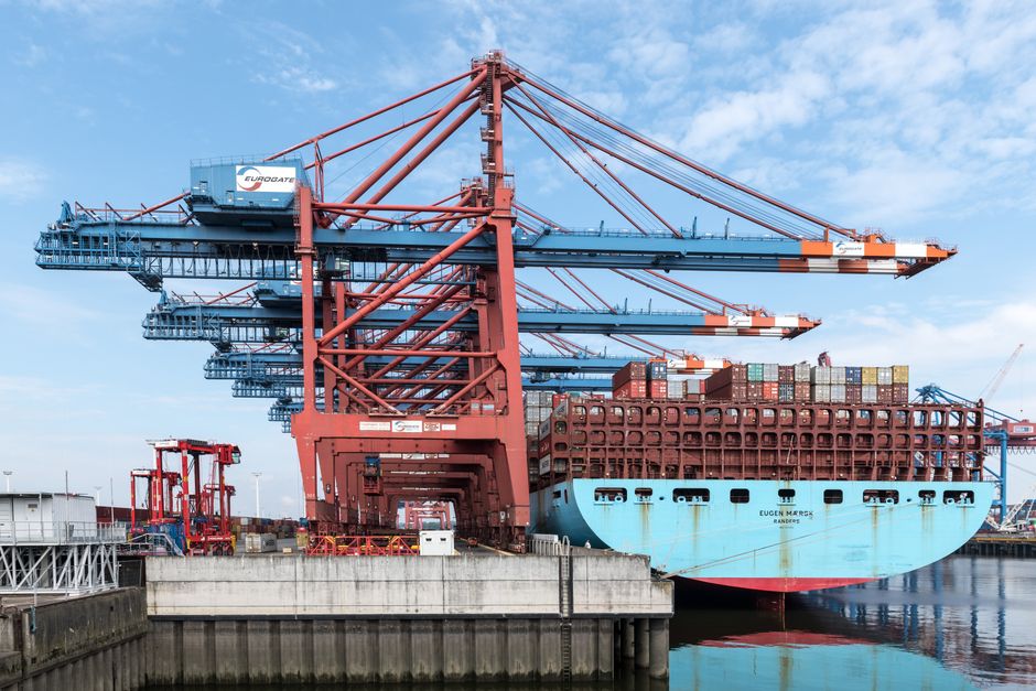 A cargo ship docked at port with gantry cranes loading shipping containers, representing trade volumes now subject to new Section 301 tariffs.