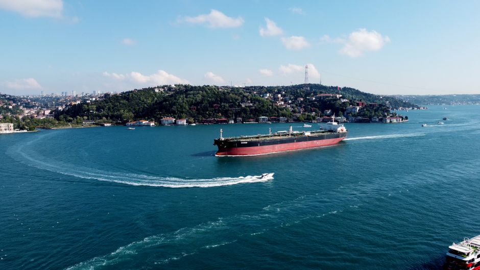 Aerial view of a large cargo ship navigating through a narrow maritime strait, illustrating commercial shipping through a critical chokepoint.