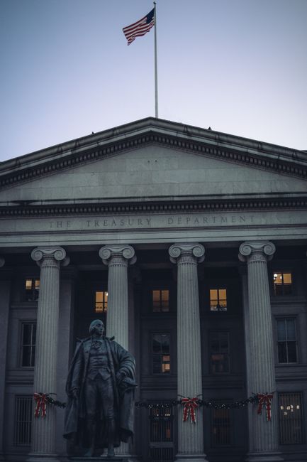 View of the US Treasury Department facade with columns and American flag at dusk.