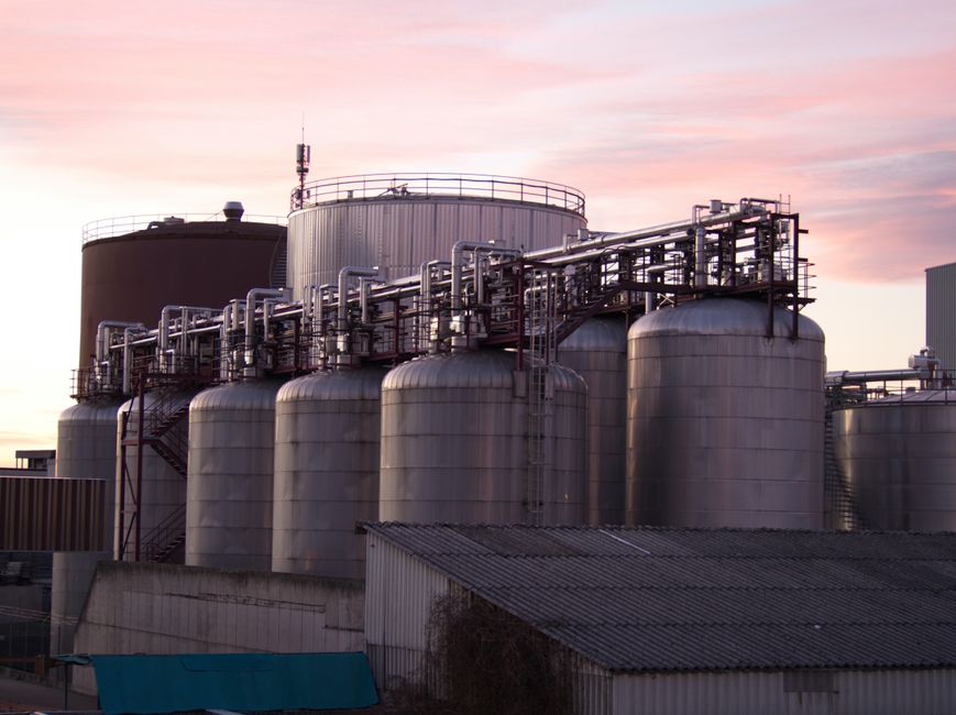 Large stainless steel oil storage tanks and pipes at an industrial refinery at sunset