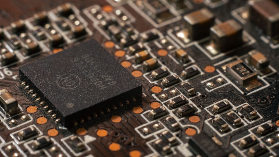 Close-up of a printed circuit board with dense electronic components and copper traces, representing semiconductor hardware.