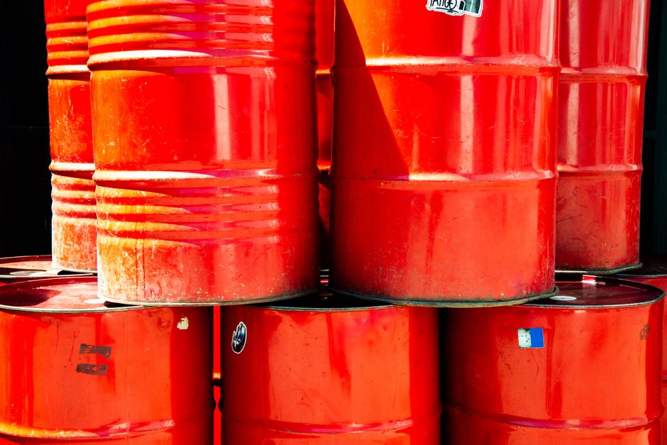 Stacked red industrial oil barrels in an outdoor storage area