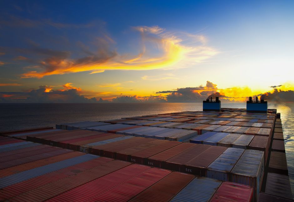 Aerial view of colorful shipping containers on a vessel against a sunset sky over the ocean