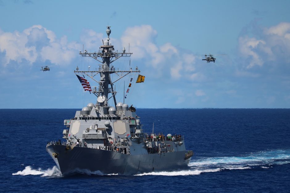 US Navy destroyer with helicopters flying overhead