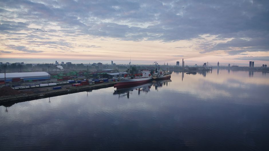 Aerial view of a large cargo port at sunrise with ships and calm water reflections