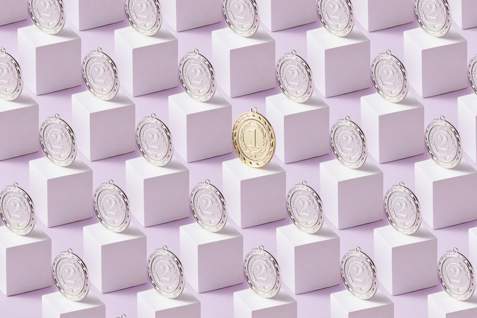 A gold medal standing out among silver medals on white display cubes.