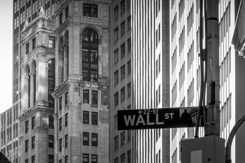 Black and white photograph of a Wall Street street sign with classic New York financial district architecture in the background.