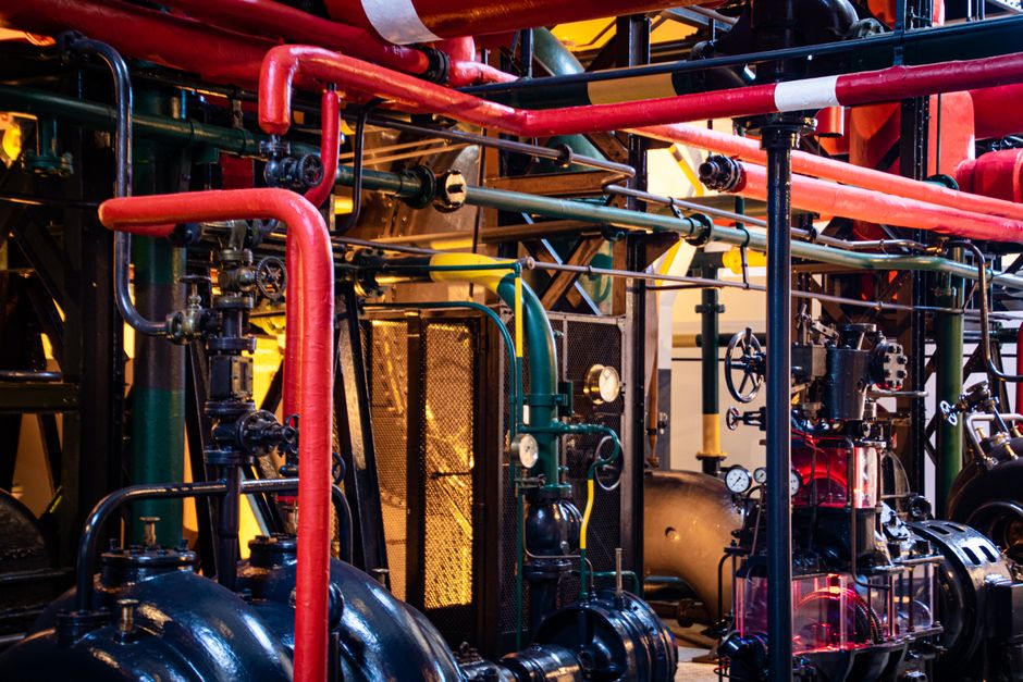 A complex network of red and gray industrial pipes and valves inside a petroleum processing facility.