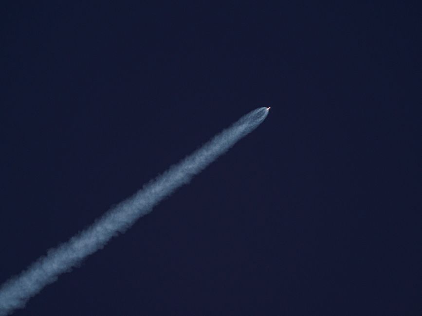 A rocket ascends into the sky, leaving a trail of smoke against the clear blue sky.