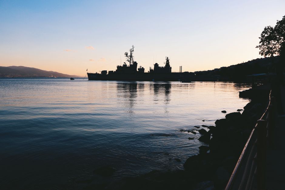Silhouette of a naval warship on calm waters at twilight, symbolizing maritime security patrols near strategic chokepoints.