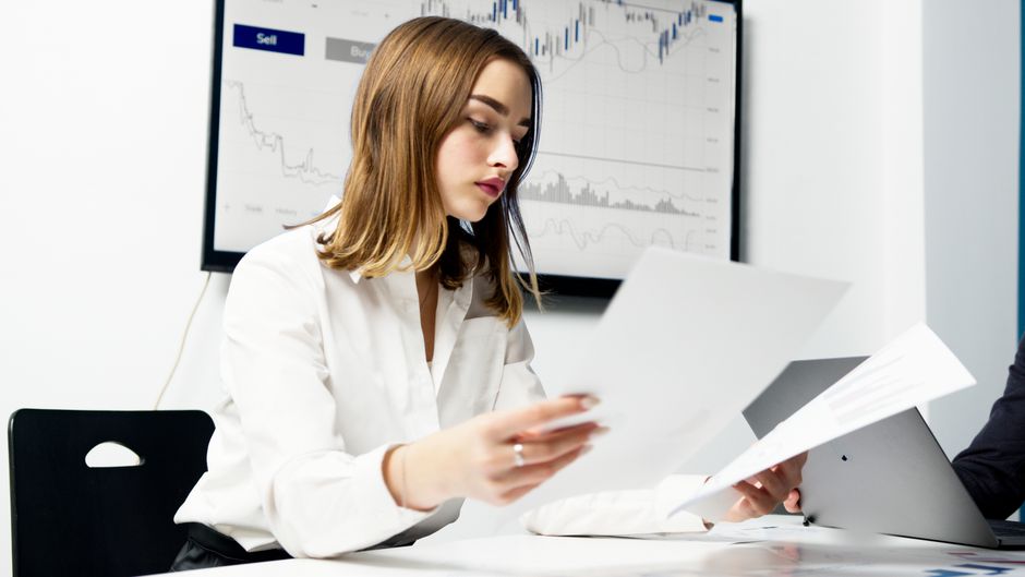 Analyst reviewing financial reports and charts in an office.